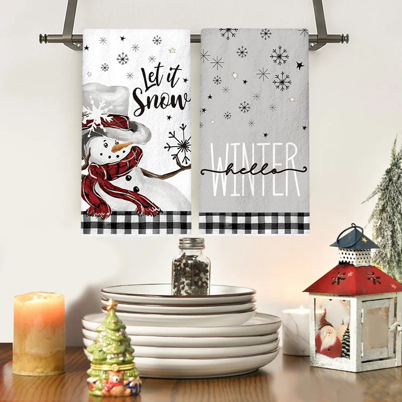 Two decorative towels with winter-themed designs hanging above a table with Christmas decor.