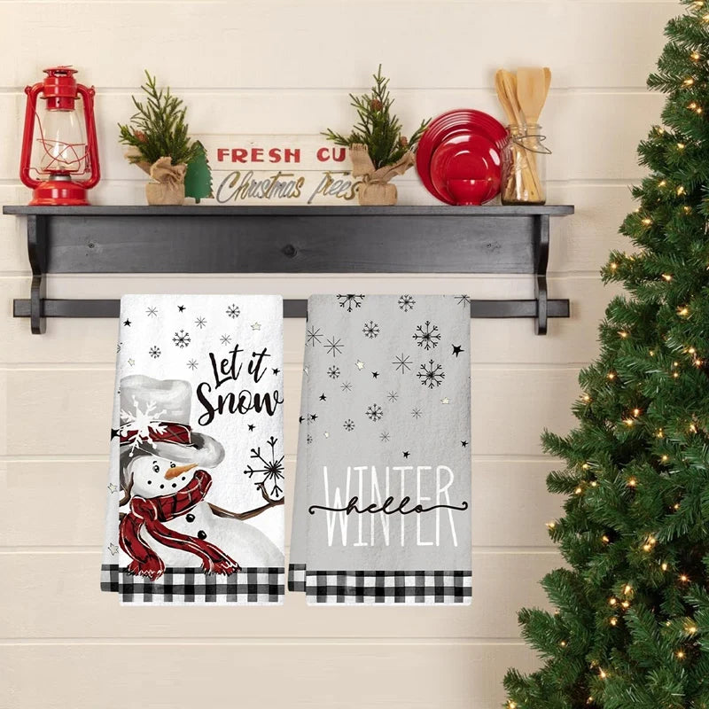 Two Christmas-themed towels hanging on a rack with a decorated Christmas tree in the background.