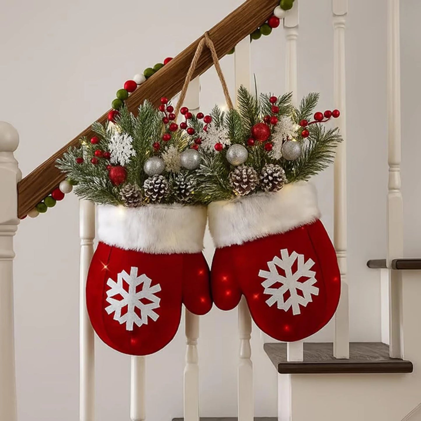 Decorative red mittens with white snowflakes hanging on a staircase, filled with Christmas greenery and ornaments.