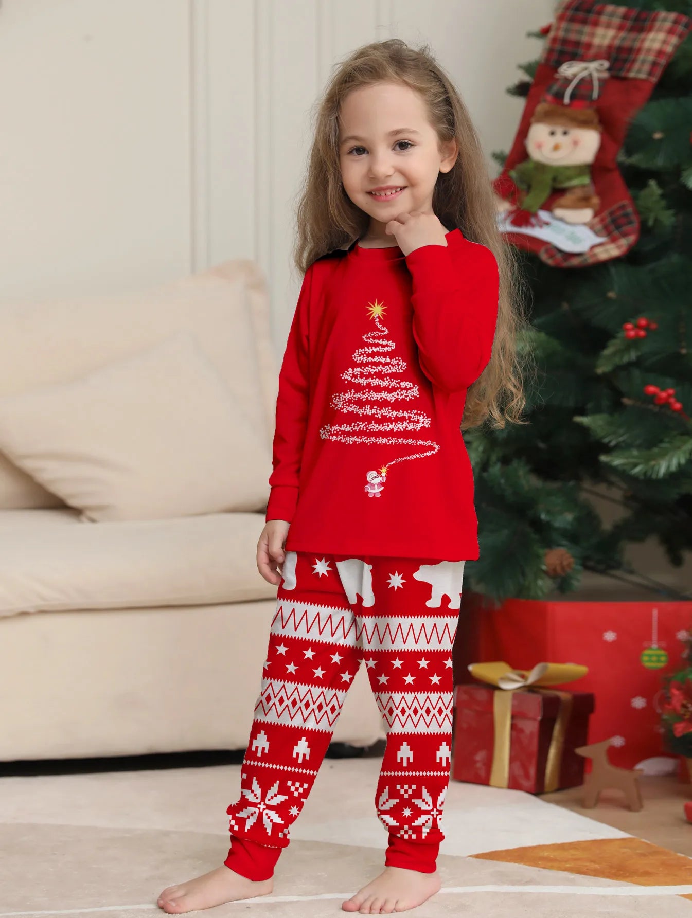 Child wearing red Christmas-themed pajamas in a festive living room.