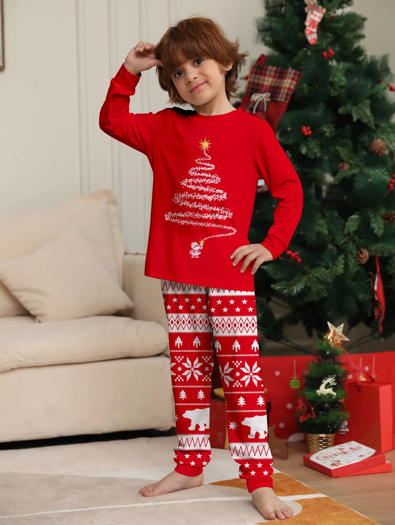 Child wearing red Christmas-themed pajamas in a living room with a decorated tree.