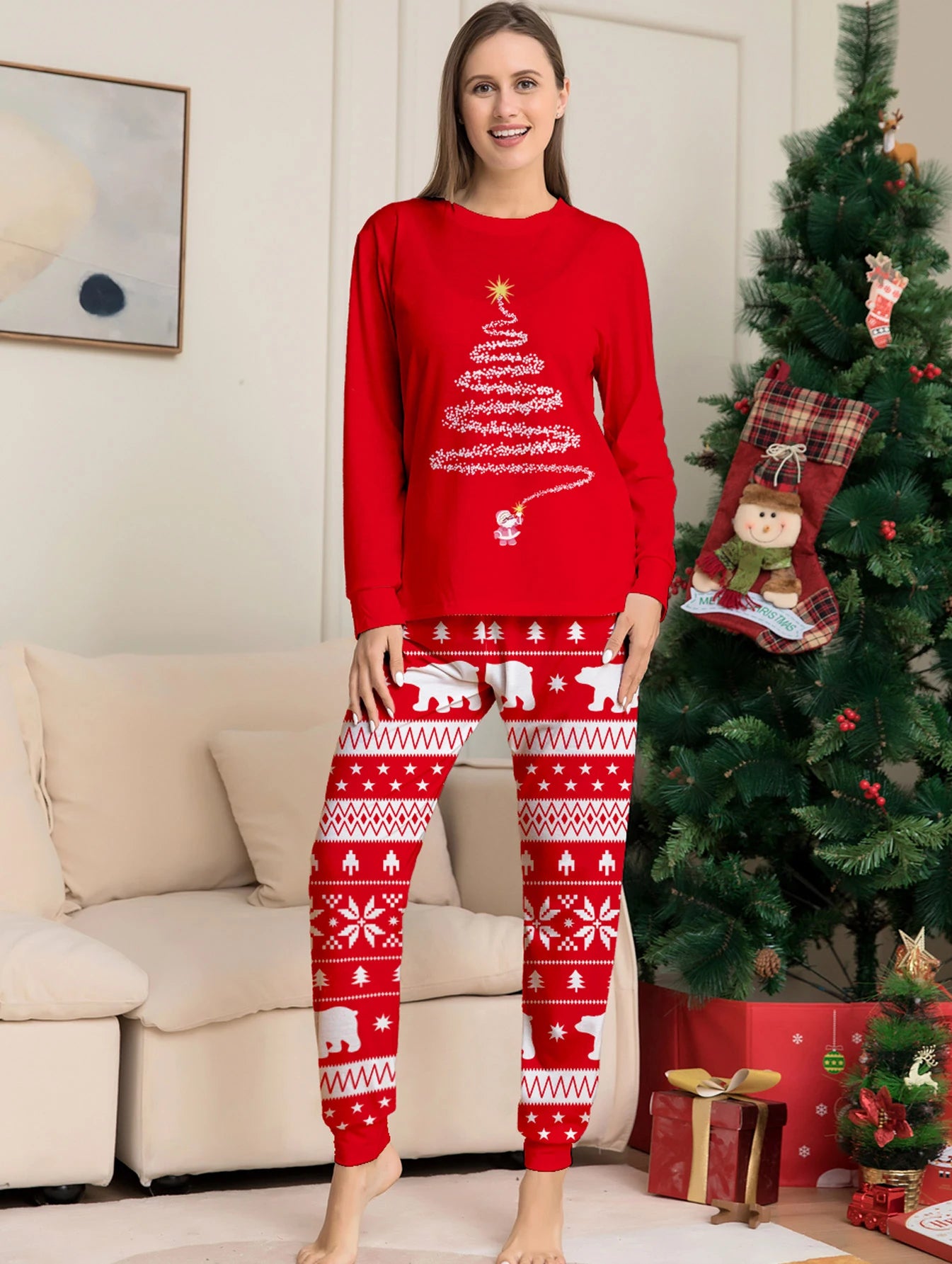 Woman wearing red Christmas-themed pajamas in a living room with a decorated tree.