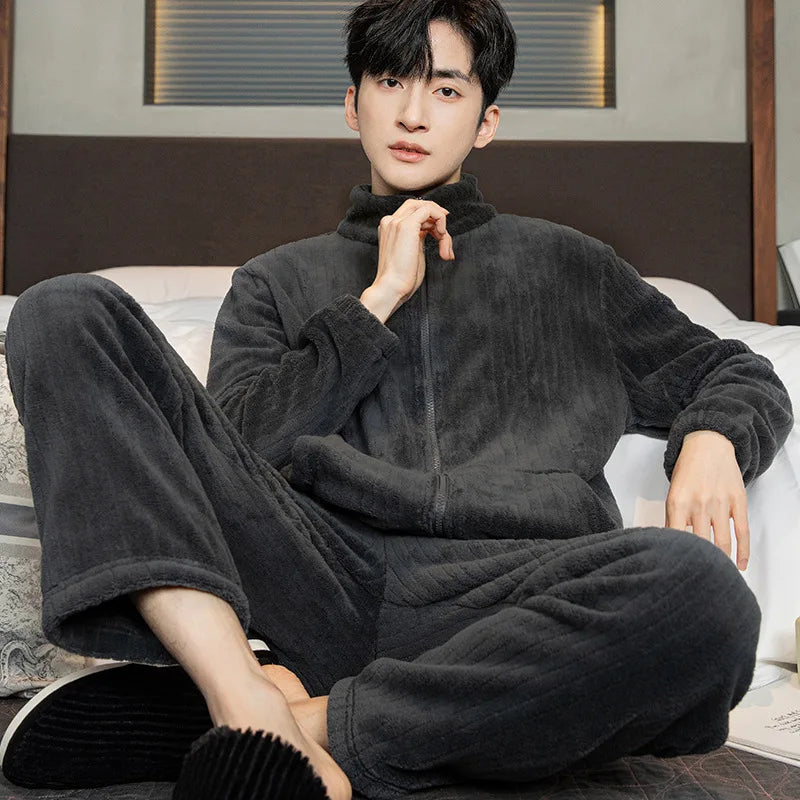Person wearing a dark gray fleece onesie sitting on a bed.