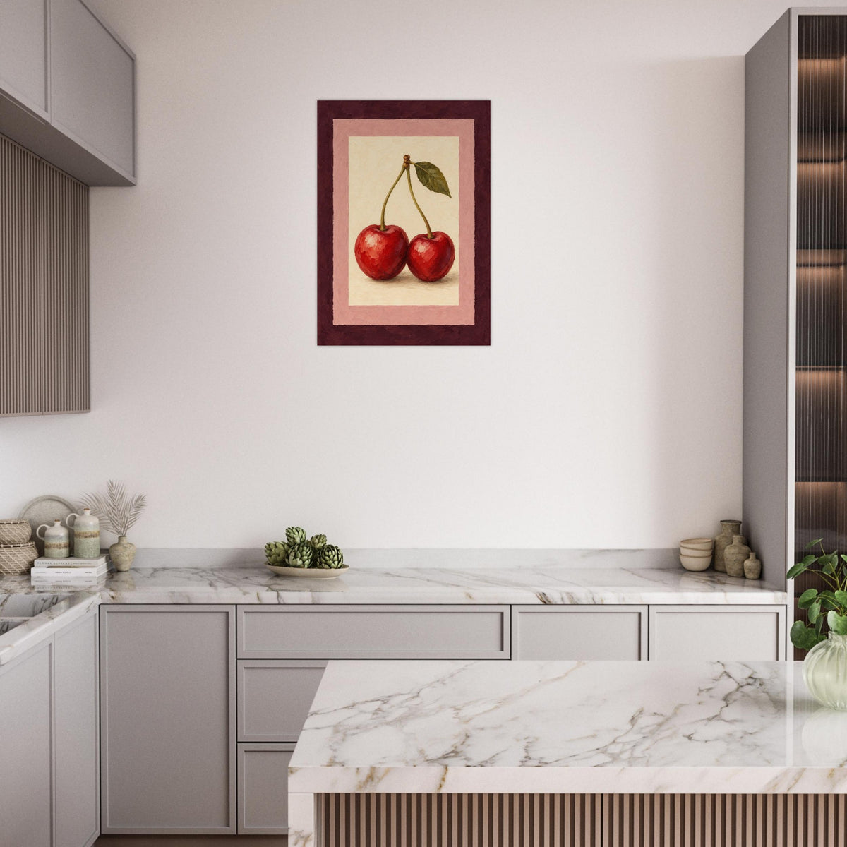 A framed wall art print depicting two red cherries on a cream background with a pink inner border and dark red frame, displayed above a marble-topped kitchen counter in a modern kitchen setting.