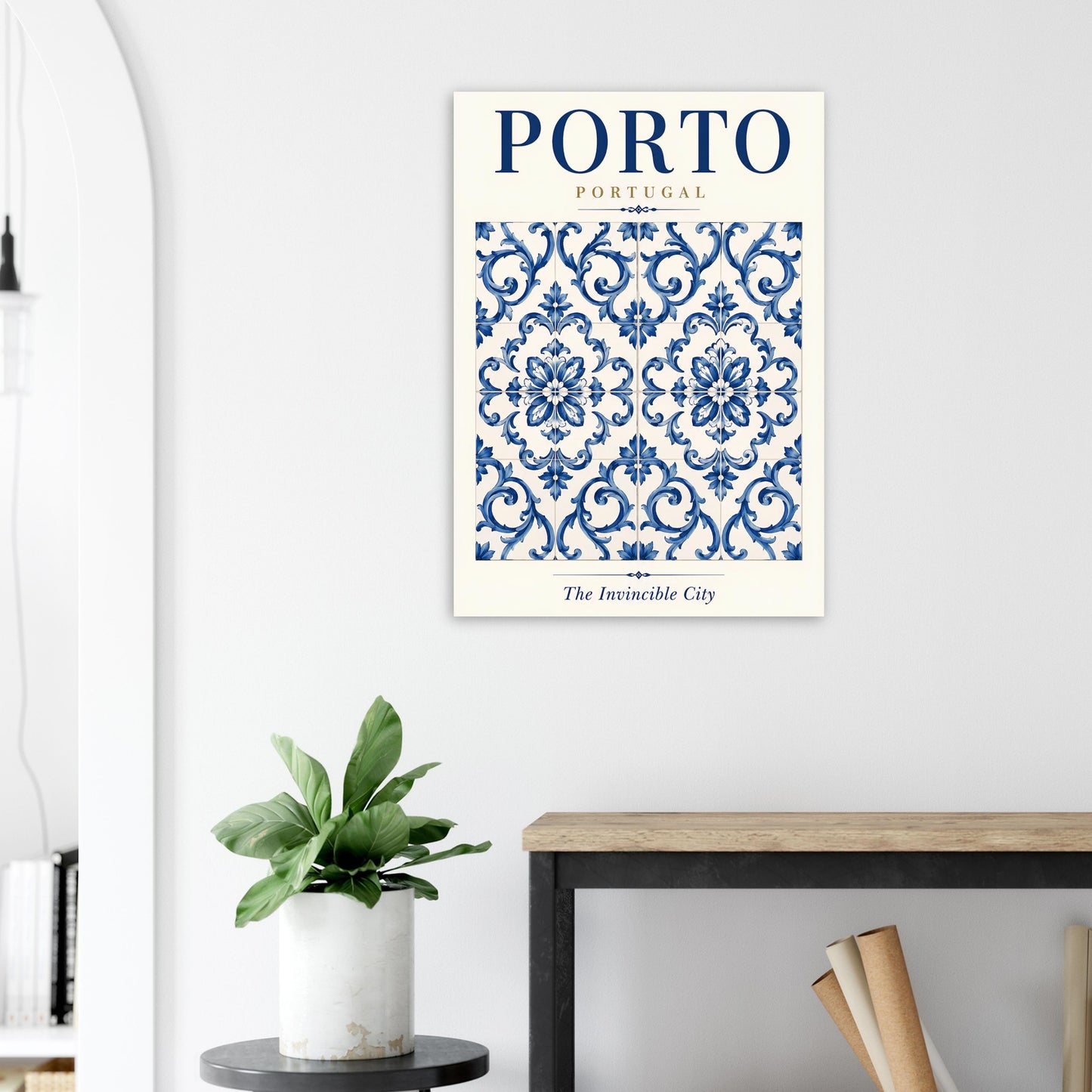 A vertical art print featuring a blue and white Portuguese damask pattern with the text 'PORTO PORTUGAL' and 'The Invincible City' at the bottom, displayed on a light gray wall above a console table with a potted plant.