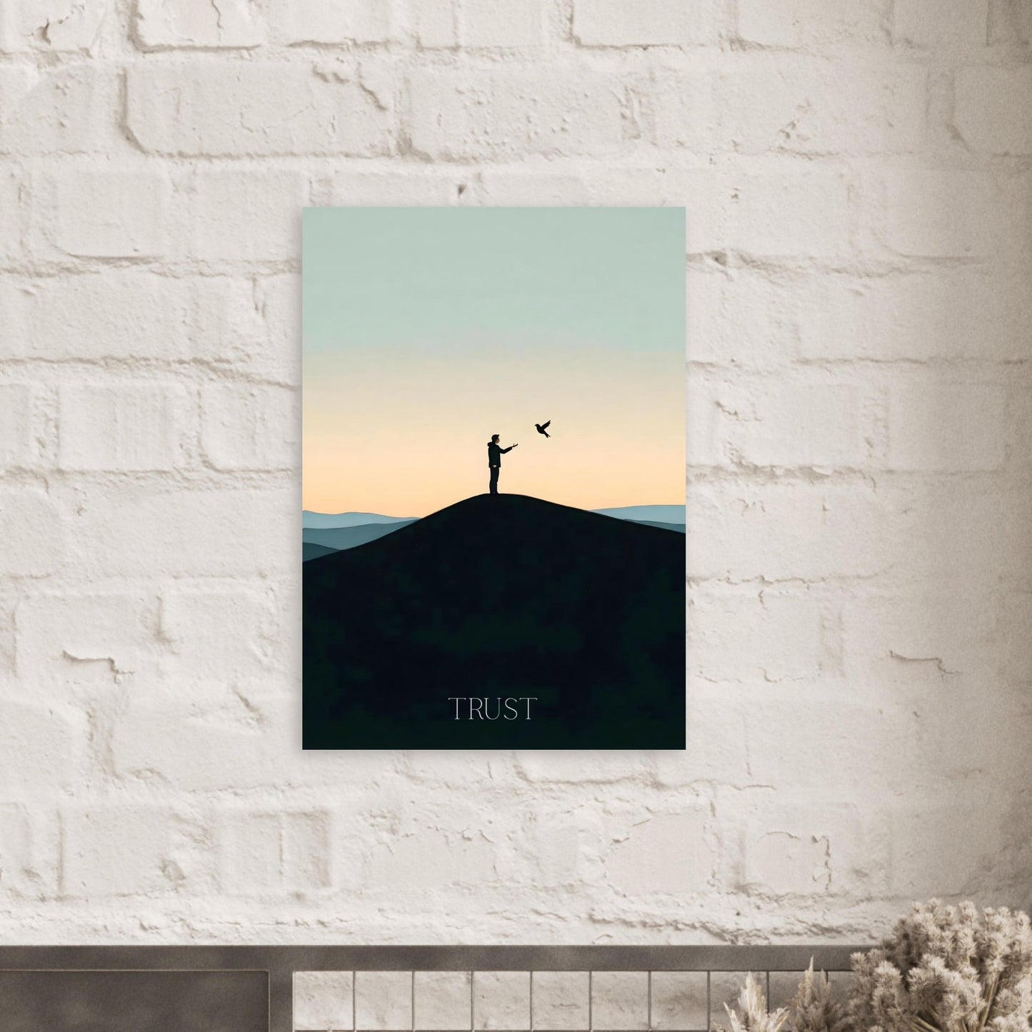 Art print of a silhouette on a hill with 'TRUST' text, hanging on a white brick wall.