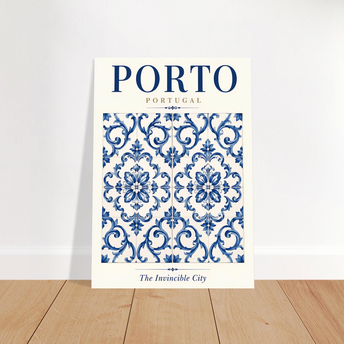 A vertical travel poster of Porto, Portugal, featuring a blue and white damask pattern with the text 'PORTO PORTUGAL' and 'The Invincible City' at the bottom, displayed leaning against a white wall on a light wood floor.