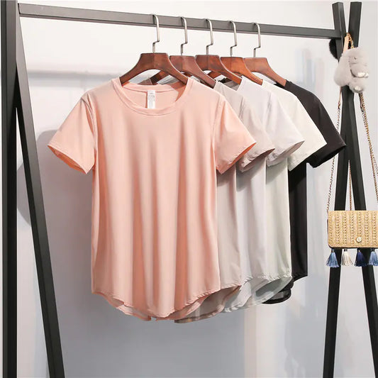 Three t-shirts in pink, white, and black hanging on a rack with a handbag in the background.