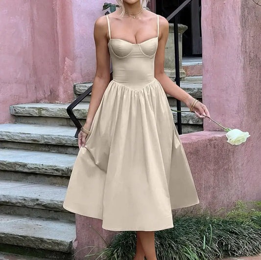 Woman in a beige dress holding a flower, standing on stone steps with a pink wall in the background