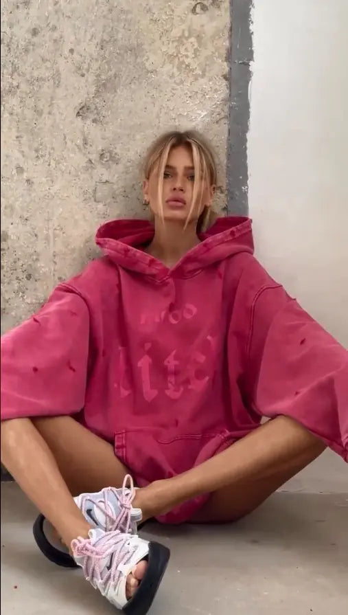 Person wearing a pink hoodie sitting against a textured wall.