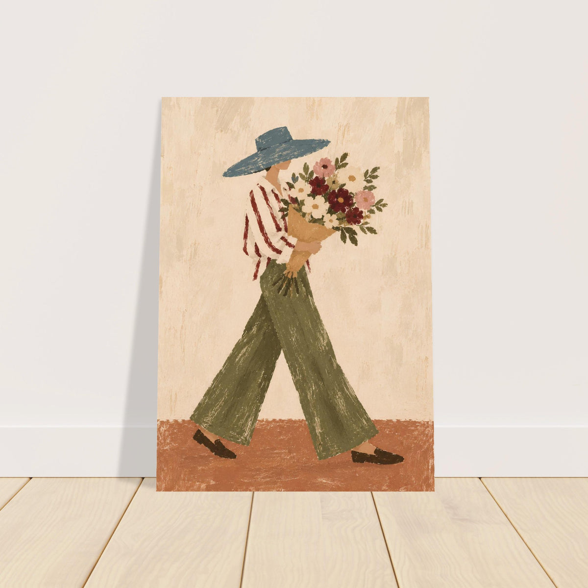 A vertical art print featuring a folk-art style illustration of a person in a blue hat, red-and-white striped shirt, and green pants carrying a bouquet of flowers, shown leaning against a white wall on a light wood floor.