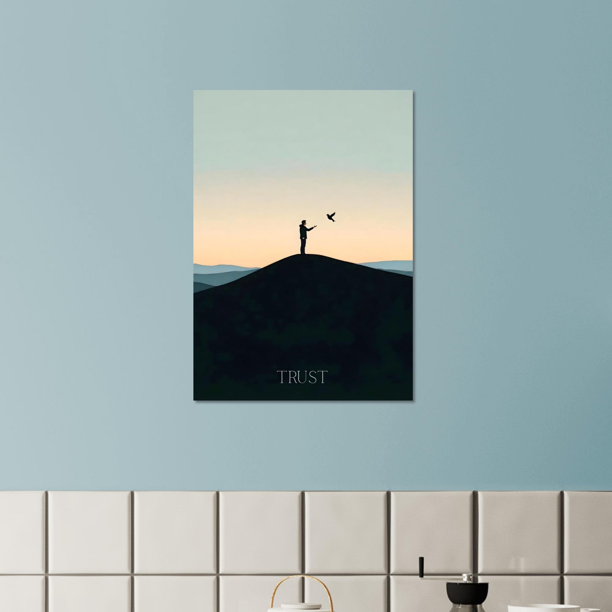 Canvas print of a silhouette on a hill with 'TRUST' text, hanging on a light blue wall above a tiled shelf.