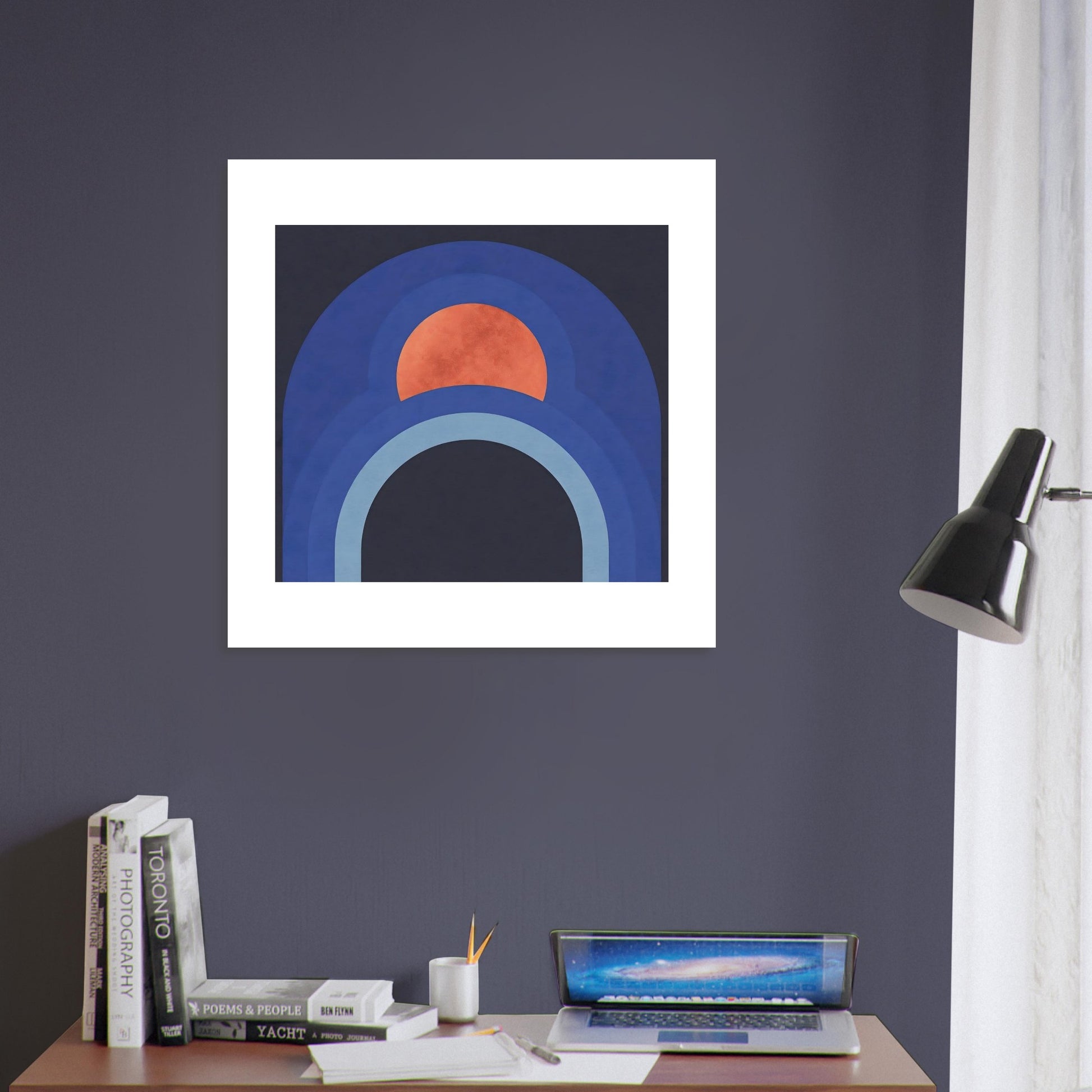 Mid century inspired blue and terracotta abstract poster displayed on a blue wall and above a small office desk with laptop and books
