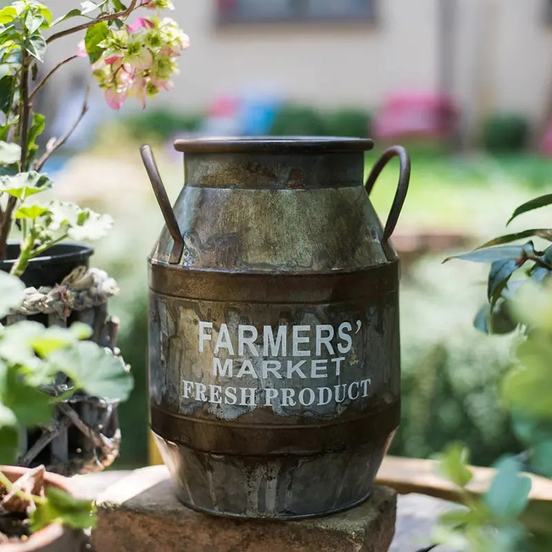 Vintage-style metal milk churn with 'Farmers' Market Fresh Product' text in a garden setting