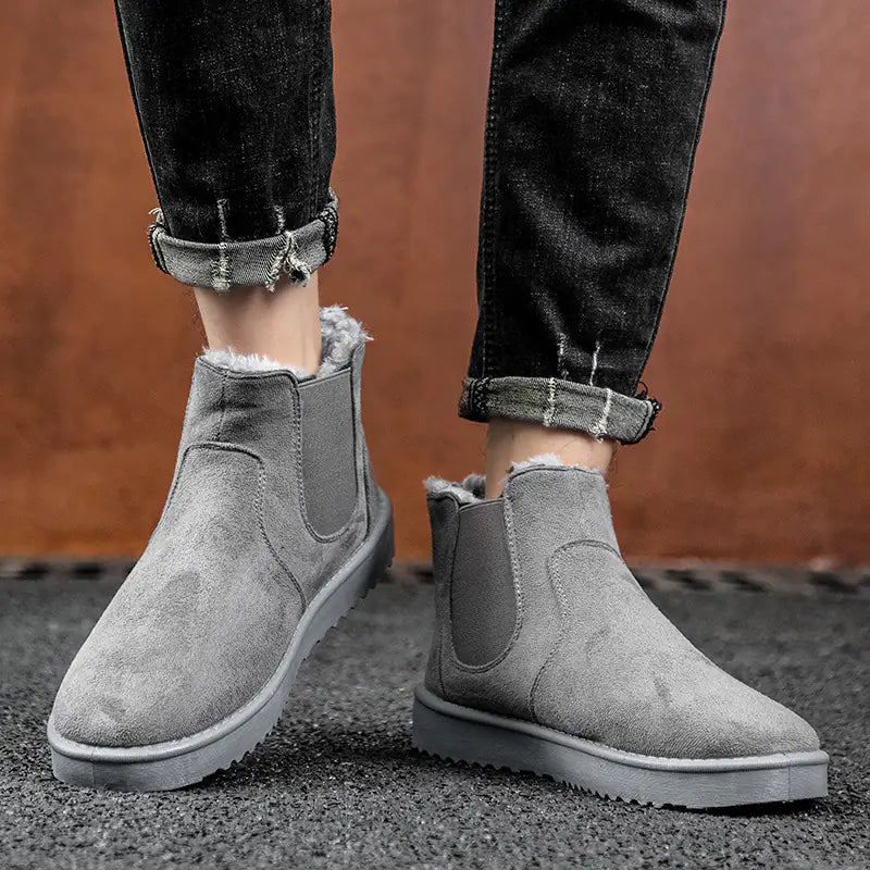 Gray suede ankle boots worn with black jeans on a textured surface.