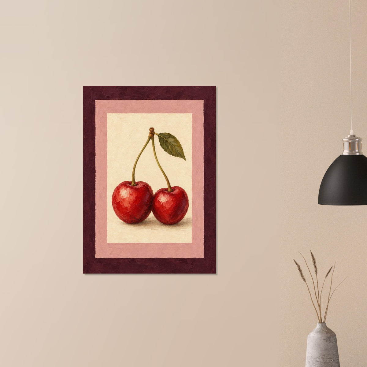 A framed art print depicting two red cherries with a green leaf, mounted on a beige wall next to a black pendant light and a small vase with dried grass.