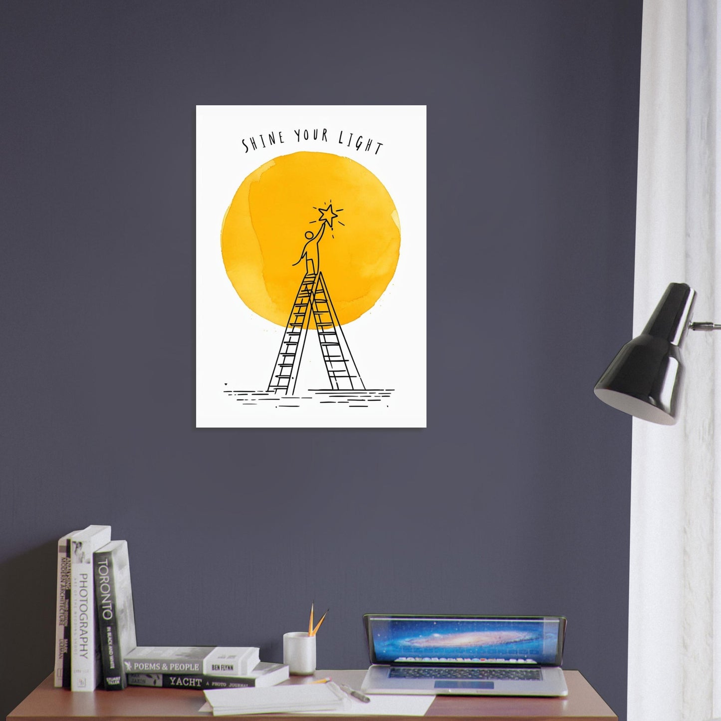 Poster with a design of a person on a ladder reaching a star, against a yellow circle with 'Shine Your Light' text, on a dark purple wall above a desk.