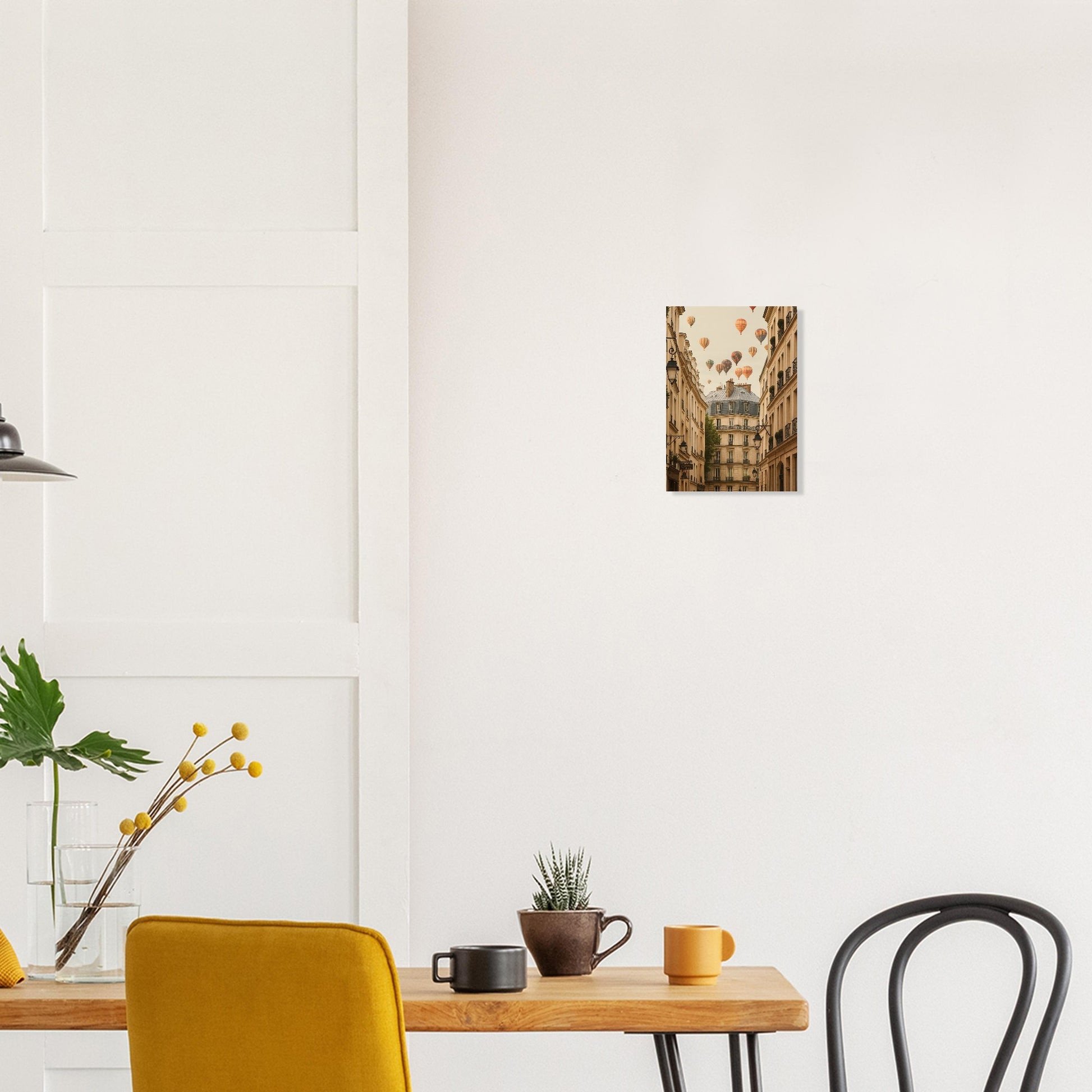 Small square painting on a white wall above a wooden table with a yellow chair and black chair.