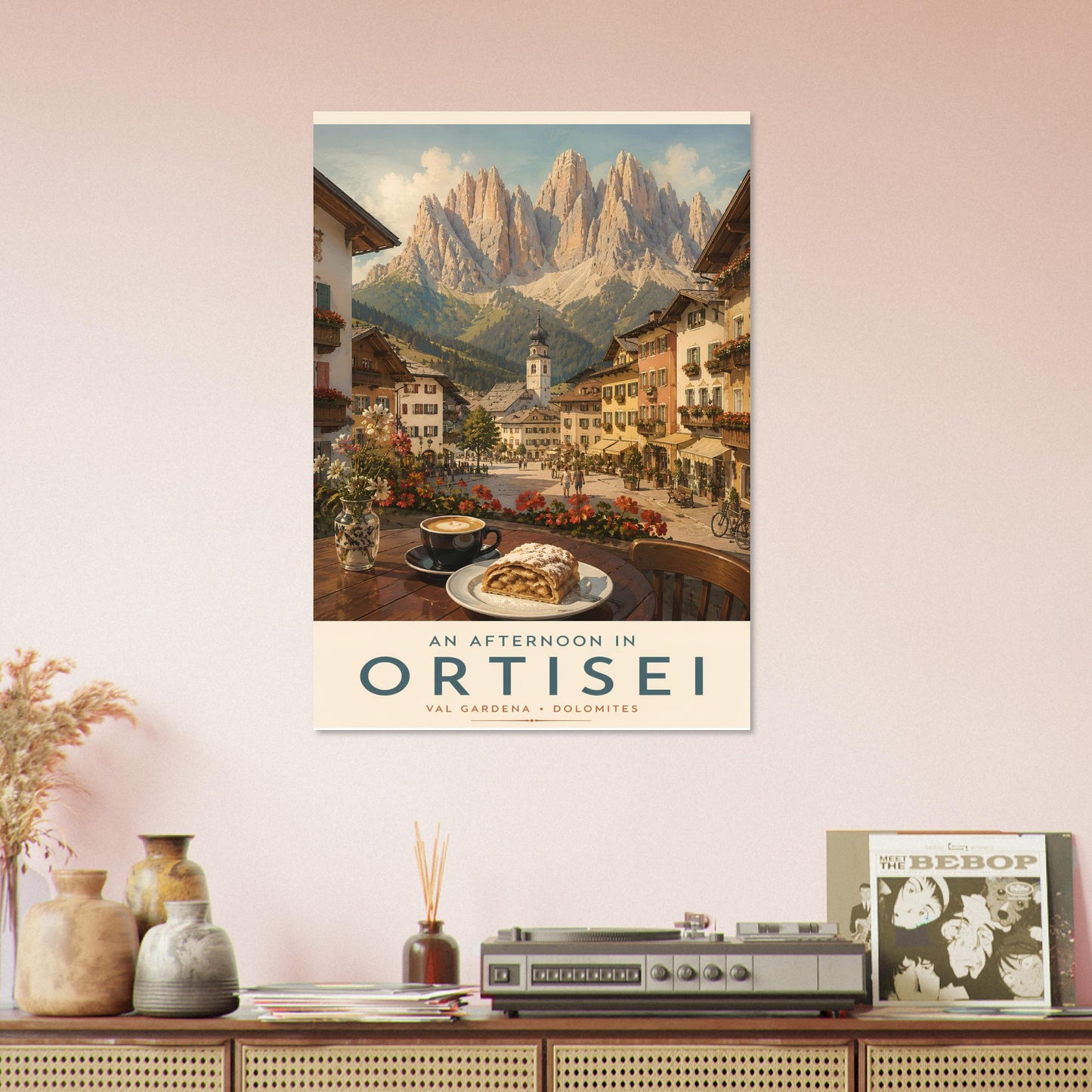 Ortisei travel poster displayed on a living room shelf arrangement, showcasing a warm afternoon view of the alpine village and surrounding mountains.