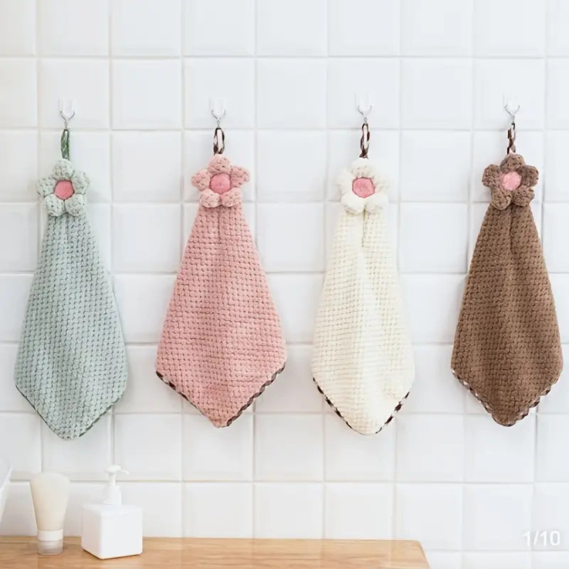 Four crocheted hand towels in different colors hanging on a tiled wall.