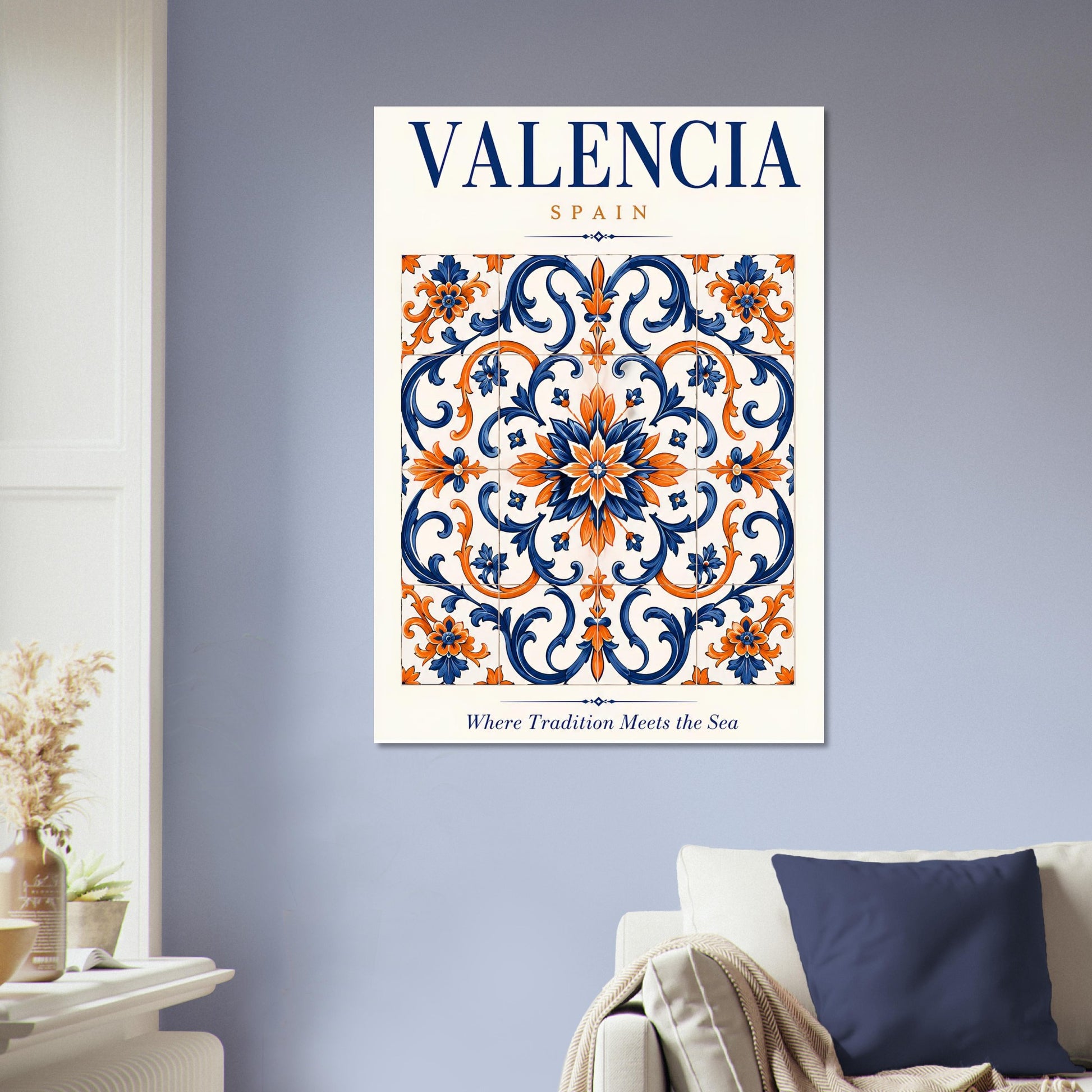 A vertical wall art print featuring a decorative Valencia, Spain tile pattern in navy blue, orange, and cream, hung on a light gray wall above a sofa in a living room setting.