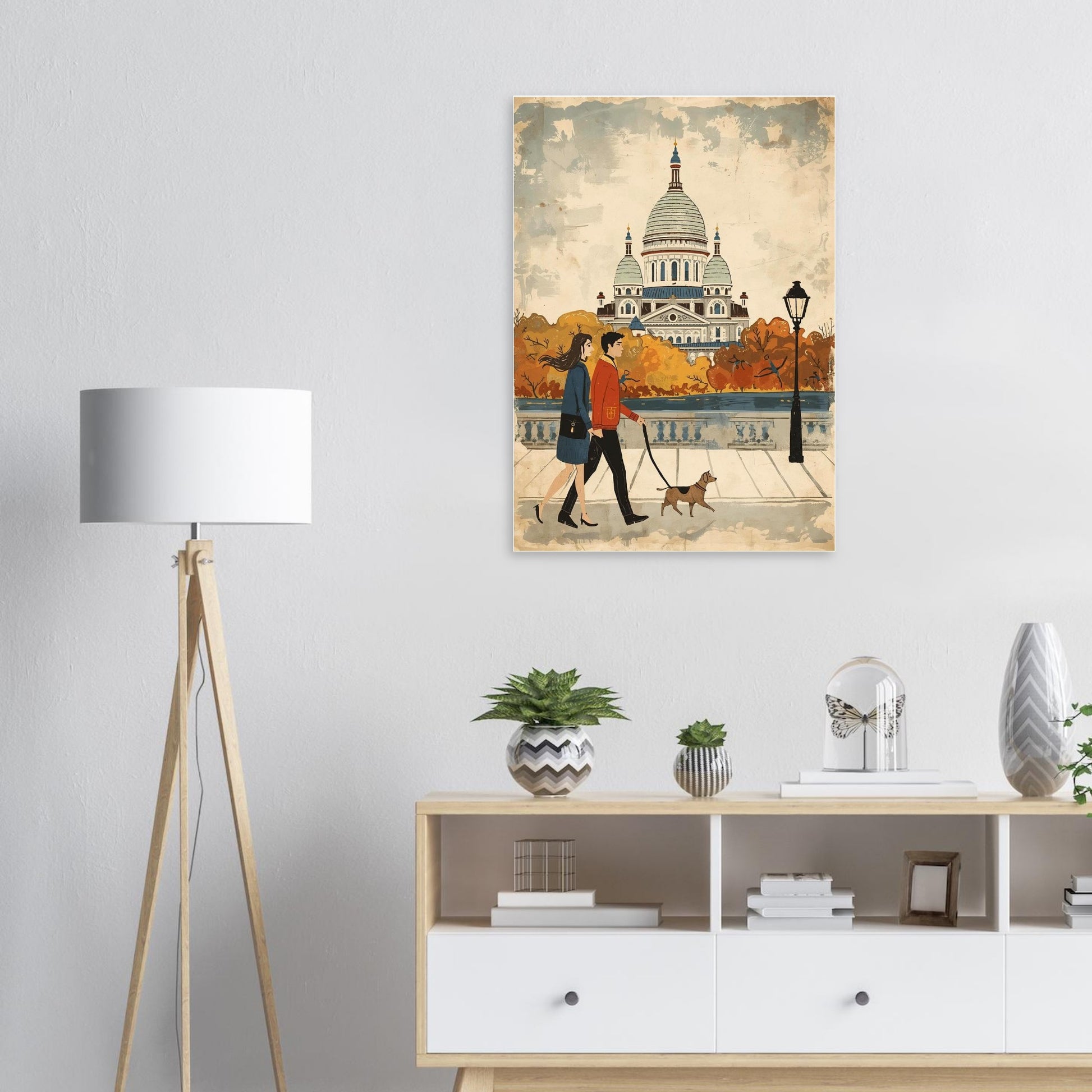 Framed artwork of a couple walking a dog in an urban setting, displayed on a wall above a white cabinet with decorative items.