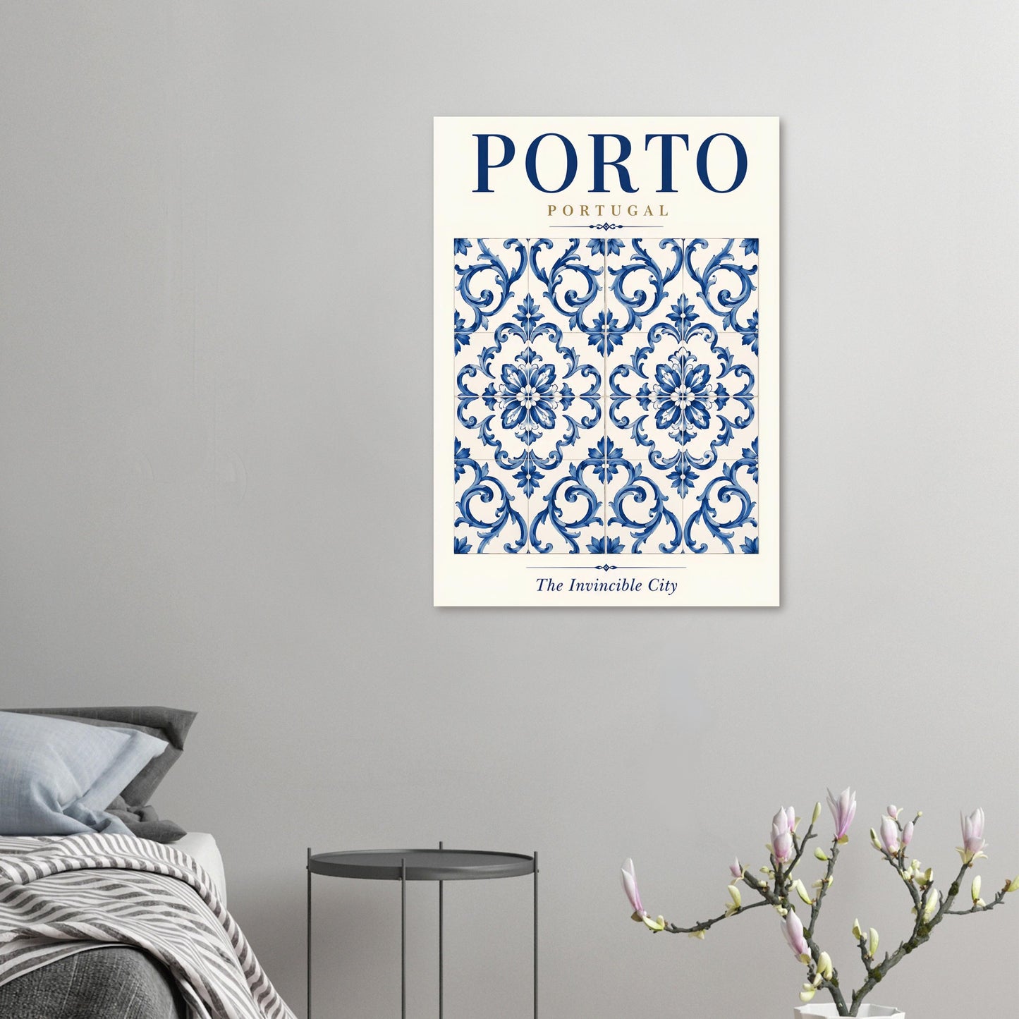 A framed wall art print featuring a blue and white damask pattern with the text 'PORTO PORTUGAL' and 'The invincible City' is shown hanging on a light gray wall above a bed and side table.