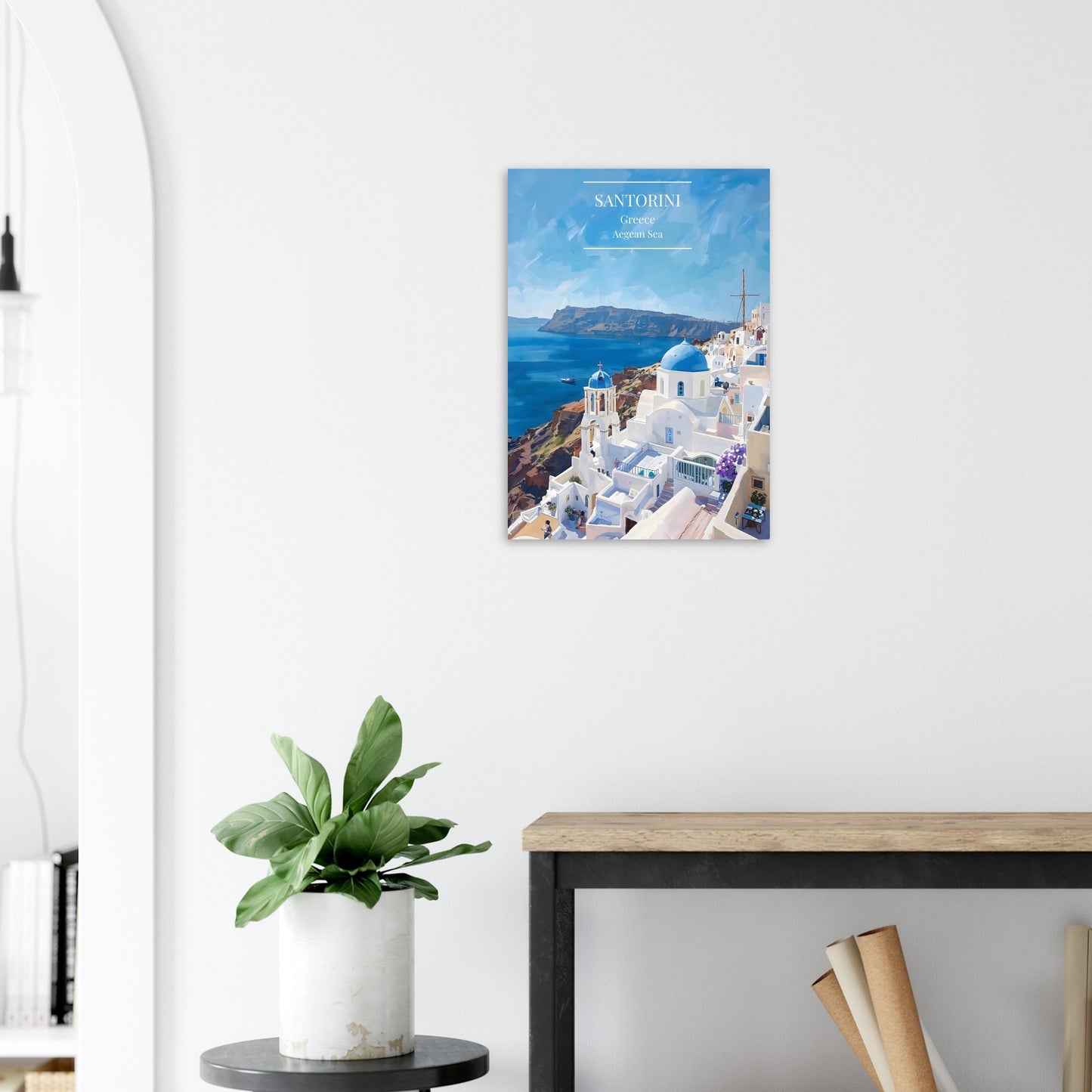 Poster of Santorini on a white wall above a wooden desk with a plant.