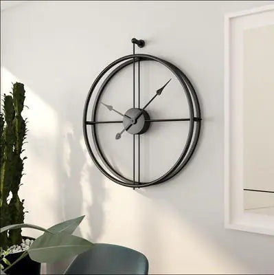 Large round wall clock on a white wall with a plant and chair in the foreground
