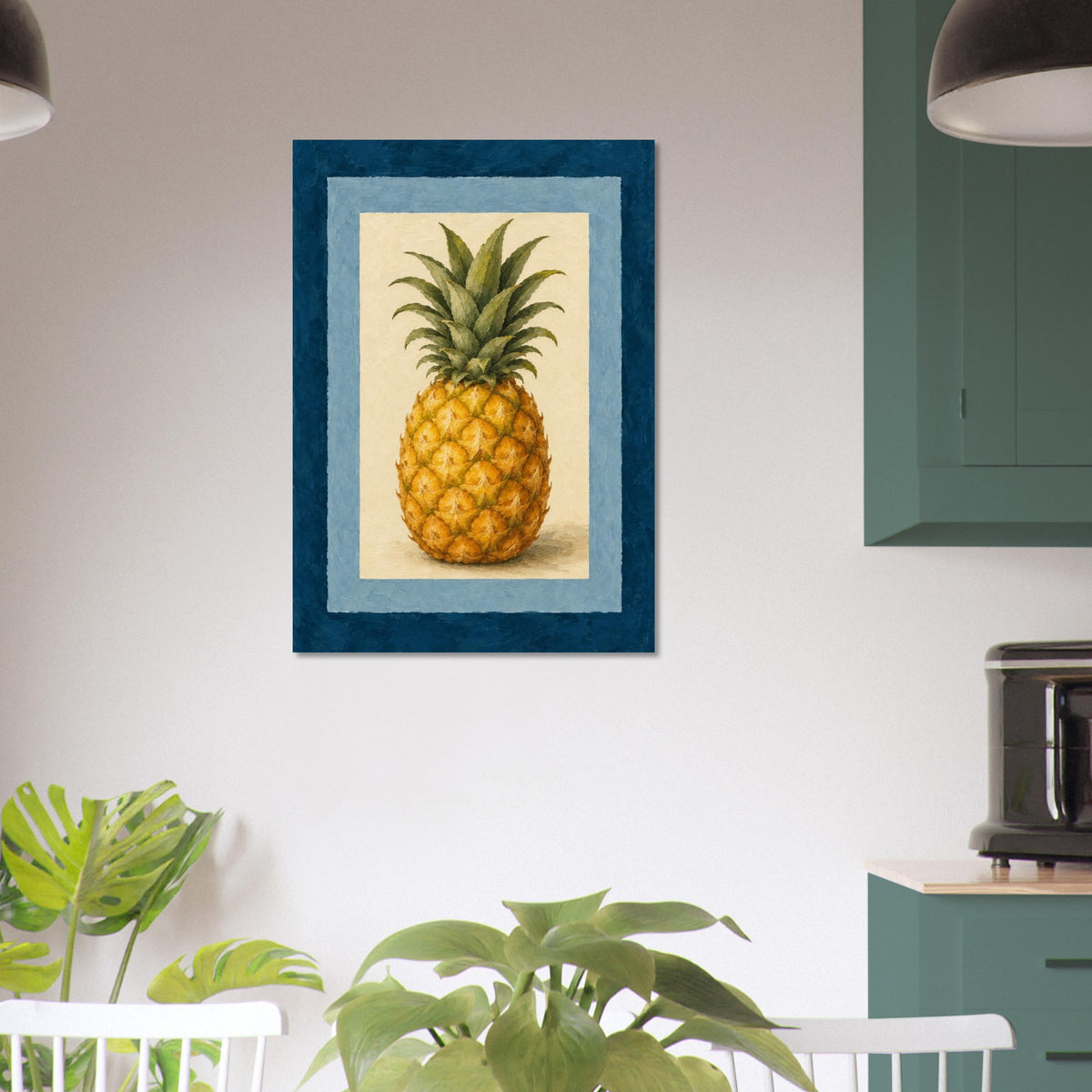 A framed botanical art print of a pineapple hanging on a white wall in a modern kitchen setting with green cabinets, plants, and dark pendant lights.