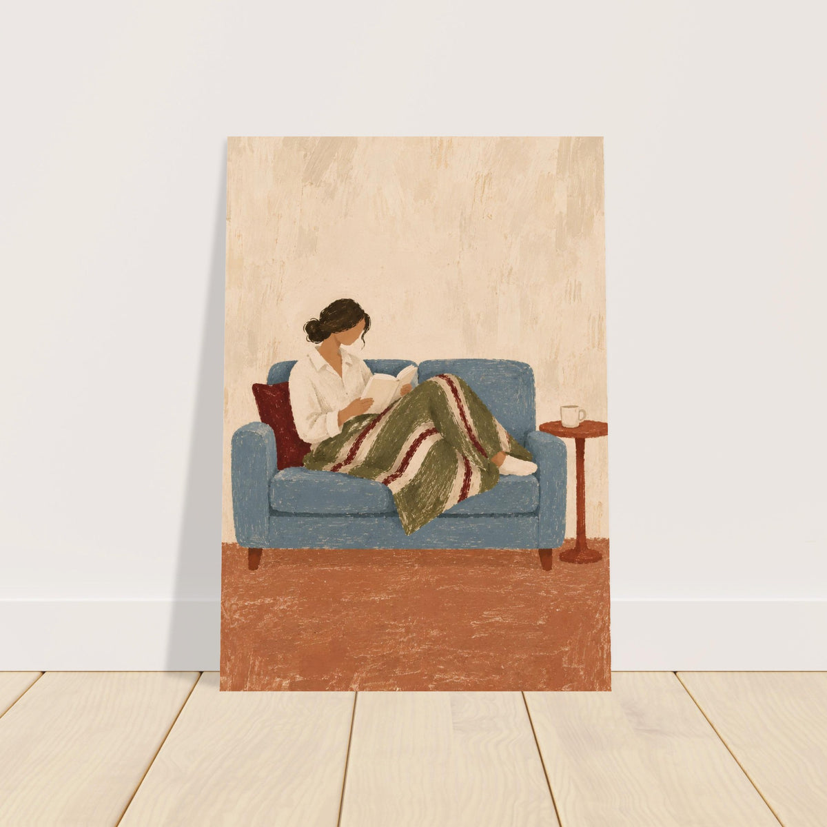 A vertical art print depicting a woman reading on a blue sofa, leaning against a white wall on a light wood floor. The print features a textured, vintage-style illustration with a beige background, blue sofa, green and red striped blanket, and a small wooden side table.