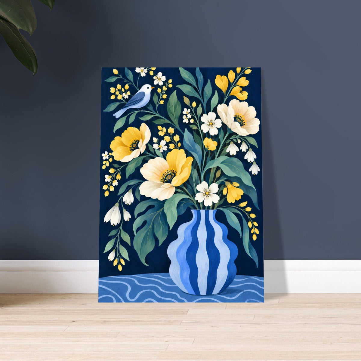 A vertical canvas art print featuring a floral bouquet in a blue patterned vase with yellow and white flowers, green leaves, and a small blue bird, displayed leaning against a dark gray wall on a light wood floor.