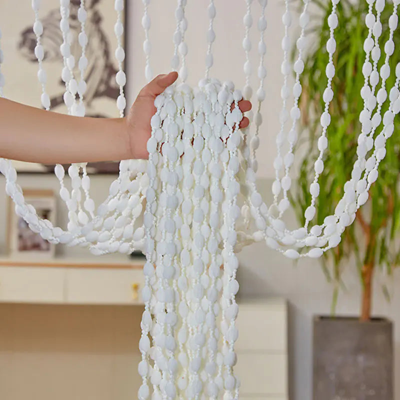 White beaded curtain with a hand holding it, indoor setting with decor elements.