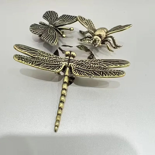 Three metallic dragonfly and insect-shaped ornaments in an antique gold and silver-tone finish, arranged on a plain light background.