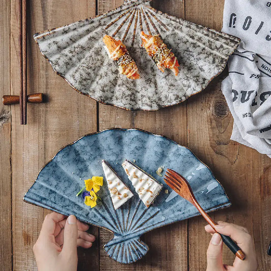 Japanese ceramic fan-shaped sushi plate with a solid glaze finish, displayed on a rustic dining table setting