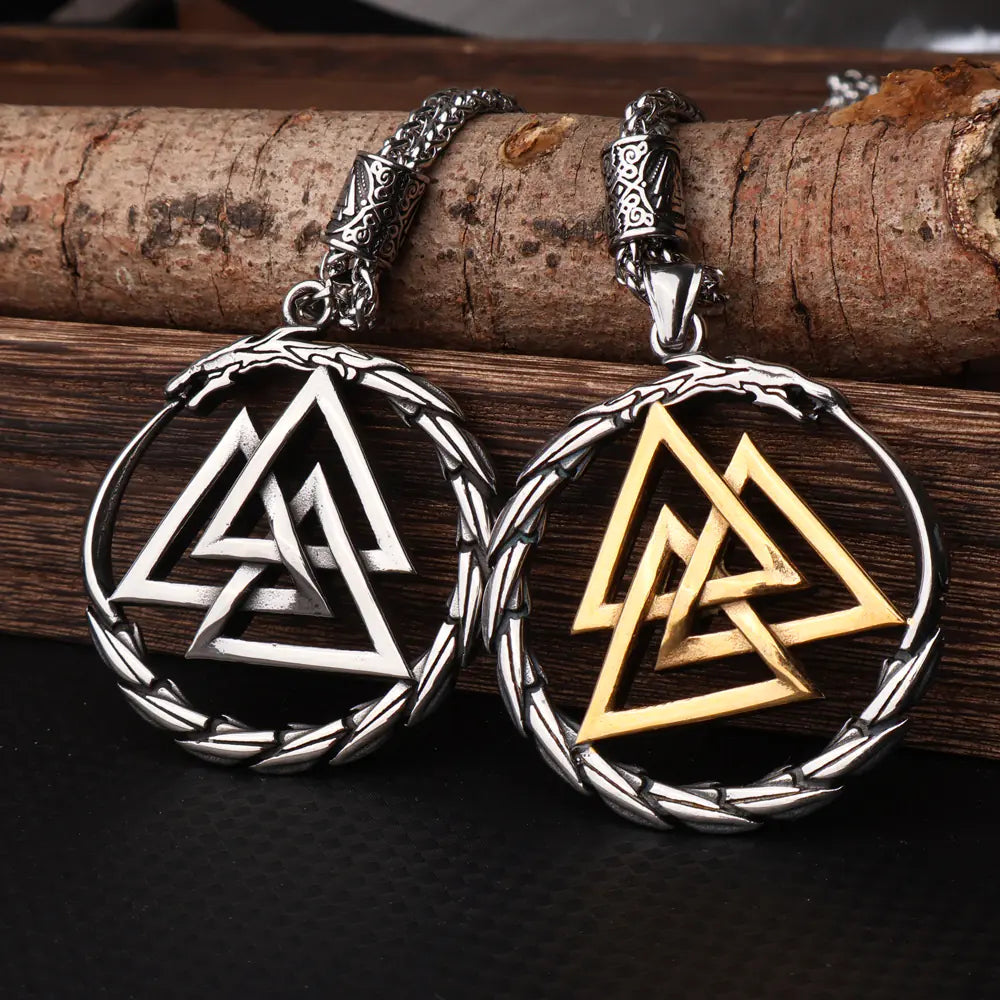 Two Viking-style necklaces, one silver and one gold, on a wooden surface.