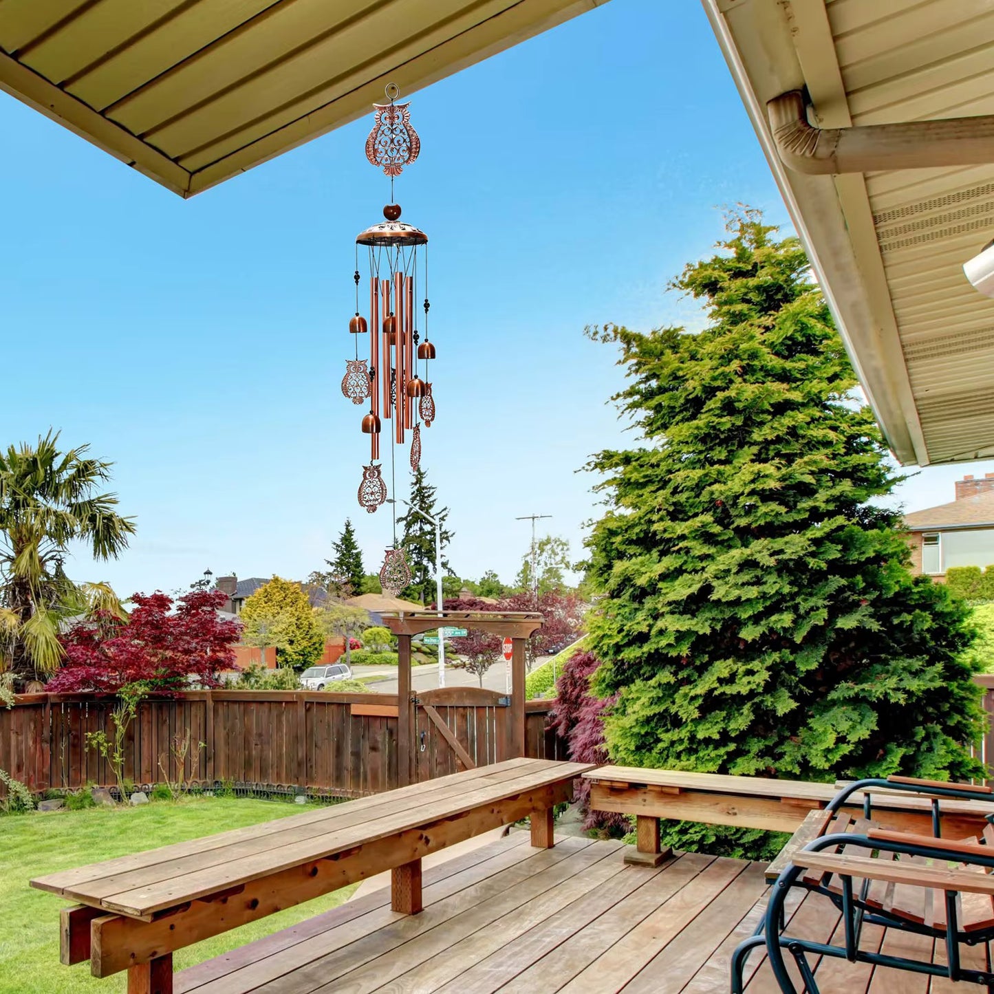 Wooden bench on a deck with a wind chime and greenery in the background
