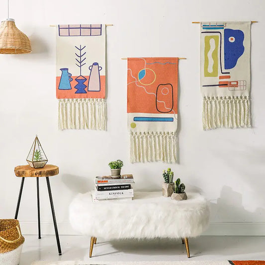 Three colorful wall hangings above a white ottoman with books and plants in a room.