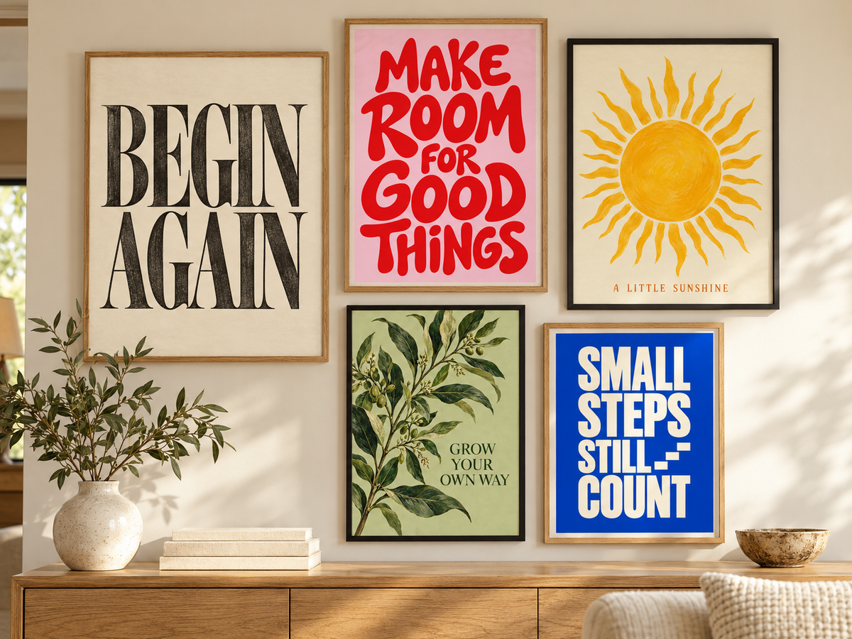 Five framed motivational and art prints displayed on a beige wall above a wooden console table. The prints feature black text on cream, red text on pink, a yellow sun on cream, green botanical leaves on olive green, and white text on blue.
