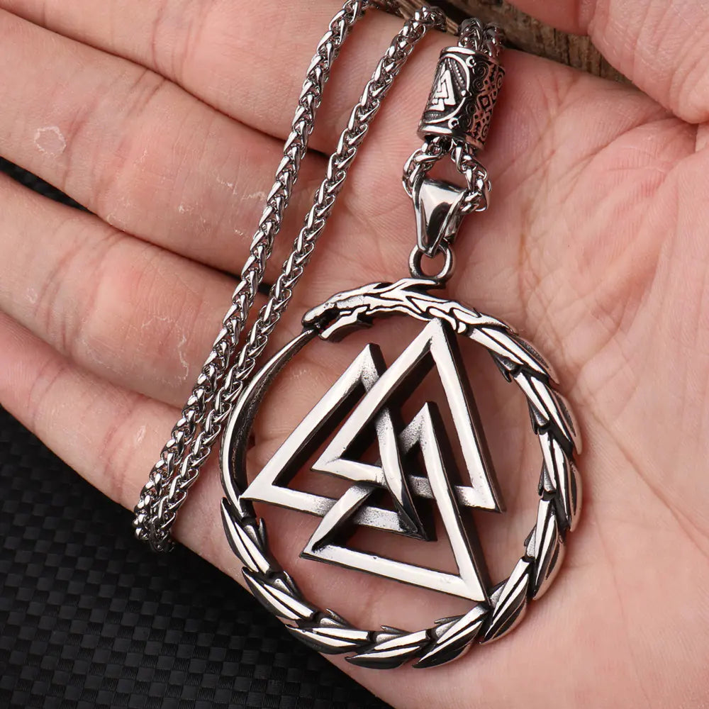 Silver necklace with a triangular pendant held in a hand against a dark background