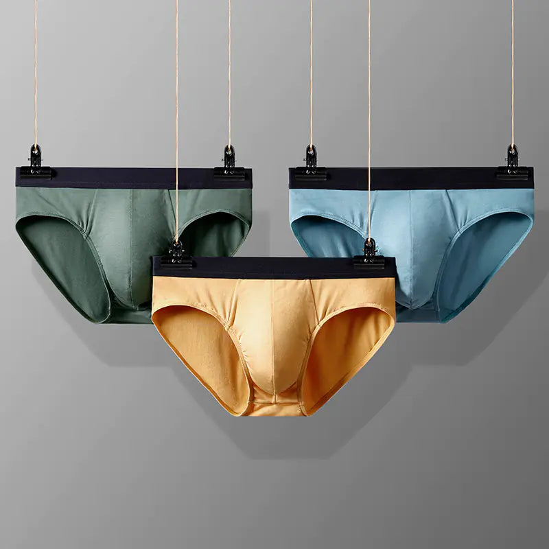 Three pairs of underwear in green, gold, and blue hanging against a gray background.