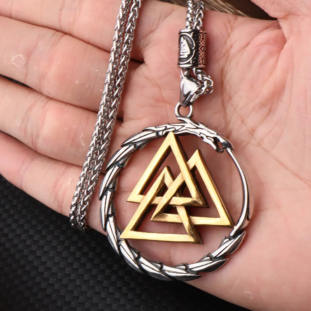 Gold Valknut pendant on a silver chain held in a hand against a black background
