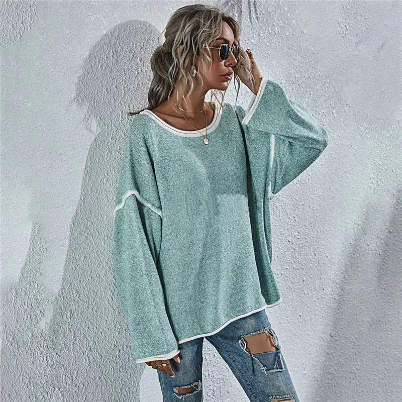 Woman wearing a light blue oversized sweater and ripped jeans against a textured white wall.