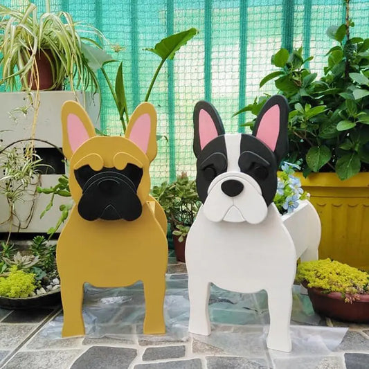 Two dog-shaped decorations, one yellow and one white, standing on a stone surface with plants in the background.
