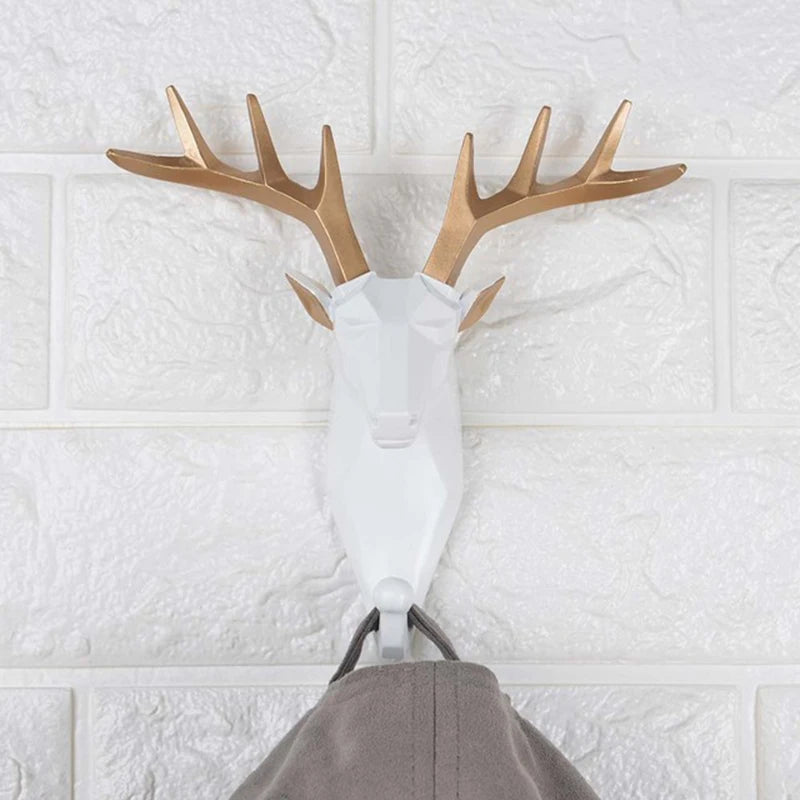 Decorative deer head hook with gold antlers on a textured white wall.