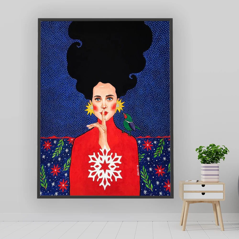 Framed artwork of a woman with a snowflake design on a blue background, placed on a white wall.