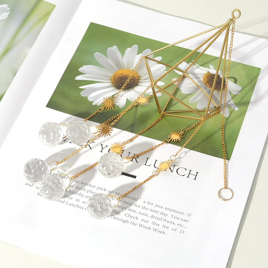 Gold geometric necklace with crystal pendants on a magazine page with flowers in the background