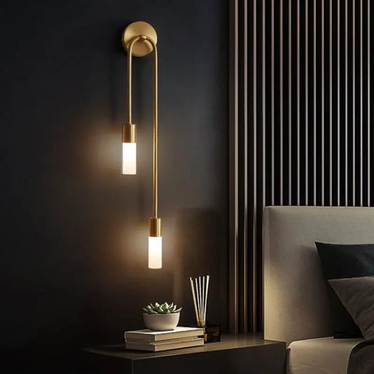 Modern wall sconce with two lights on a dark wall next to a bed.