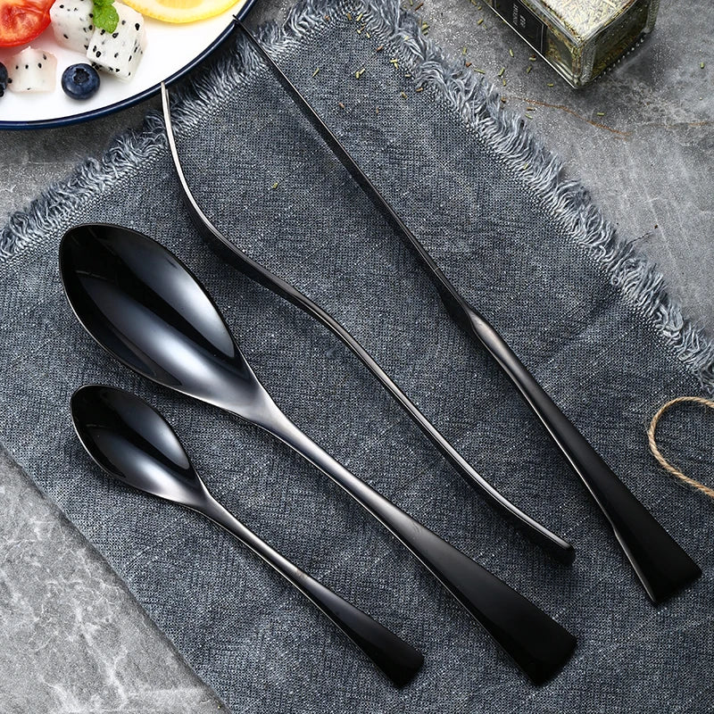 Set of black spoons on a textured gray surface with a plate of fruit in the background.