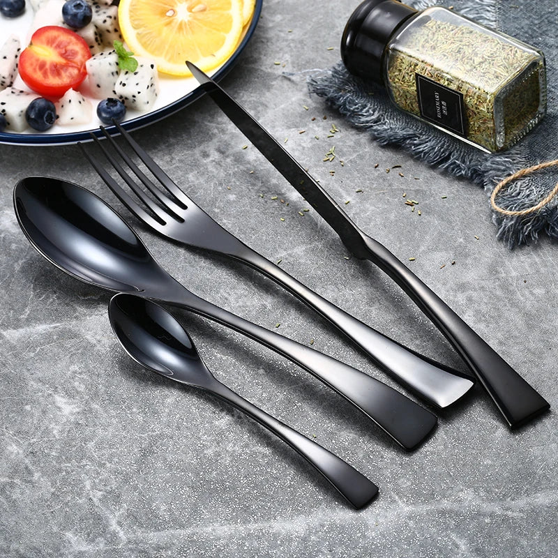Set of black cutlery including spoon, fork, and knife on a gray surface with a plate of salad in the background.